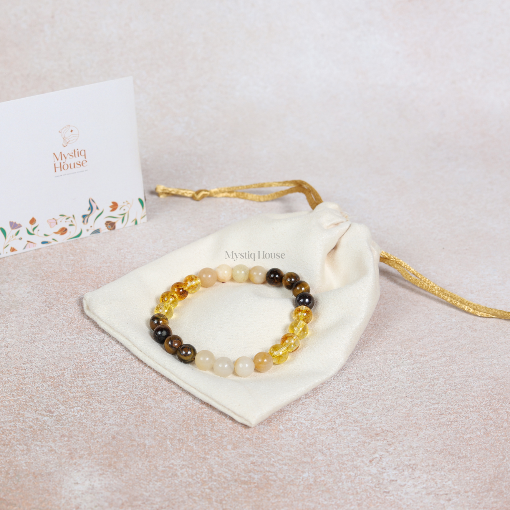 Beaded bracelet on a white drawstring bag with 'Mystic House' branding, on a light beige background.